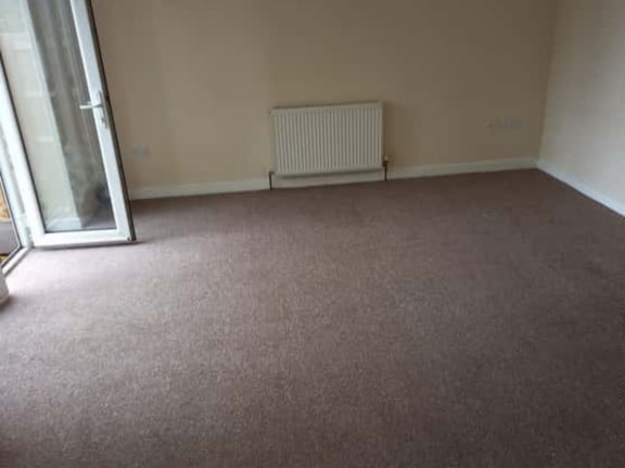 This is a photo of a living room after it has been cleaned. The room is empty and has a brown carpet that has been steam cleaned works carried out by Clerkenwell Carpet Cleaning